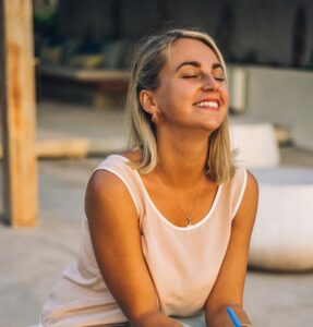 a smiling woman sitting | To be yourself in a world that is constantly trying to make you something else is the greatest accomplishment.